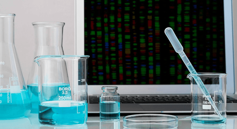 AI Chemistry Platforms ROI Laboratory glassware with blue liquid positioned in front of a laptop displaying genetic data.