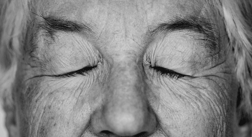 Cellular Aging And Longevity Close-up black and white portrait of an elderly person's face with deep wrinkles and closed eyes.